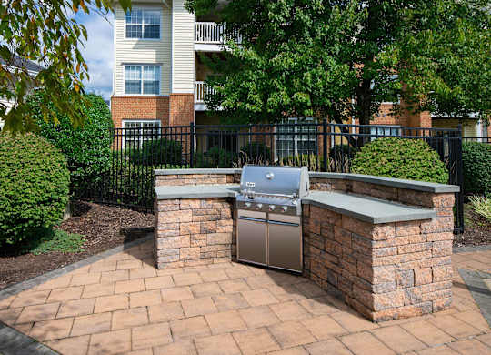 A brick BBQ grill is in the middle of a brick patio.