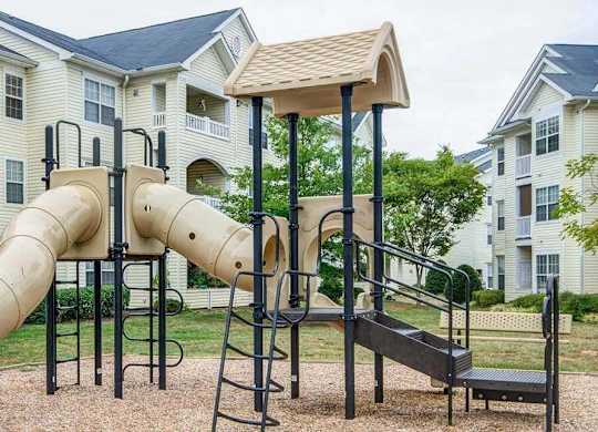 A playground with a slide and a climbing frame in front of apartment buildings.