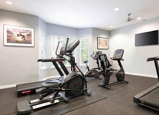 A room with a treadmill, elliptical trainer and a stationary bike.