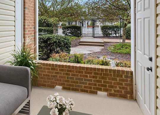 A grey sofa sits on a patio with a brick wall and a white door.