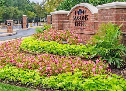 A brick wall with a sign that says "Masons Keep" in front of a parking lot.