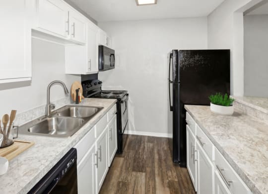 Model apartment kitchen with white cabinets and a black refrigerator