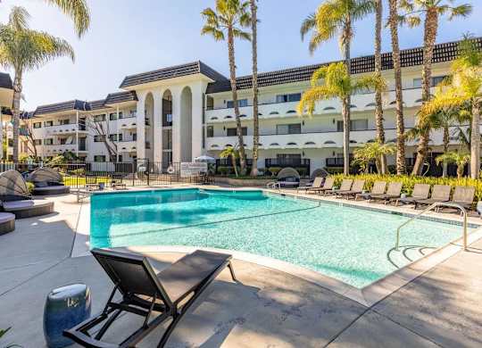 A pool surrounded by palm trees and lounge chairs.