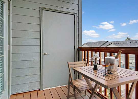 A wooden table with two chairs is on a deck with a white door on a patio.