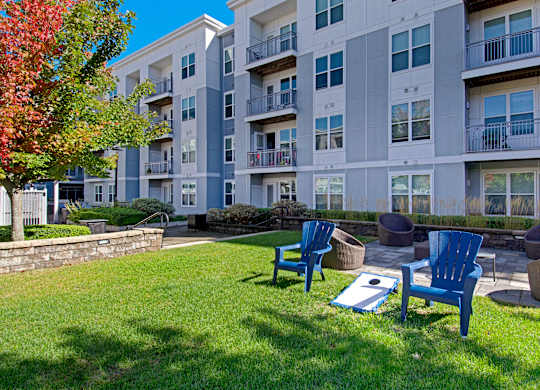 A sunny day at a grassy courtyard with blue chairs and a white building in the background.