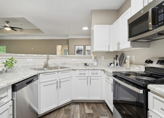 Model apartment kitchen with white cabinets and a stove and a microwave