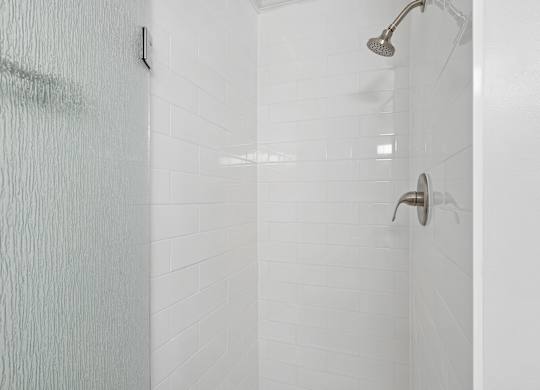 A white tiled shower with a shower head and hand held shower.