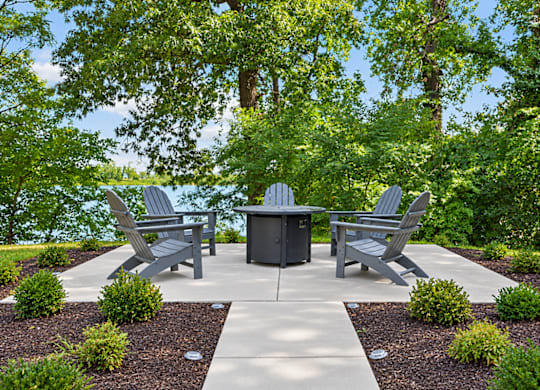 A concrete patio with a table and chairs surrounded by greenery.