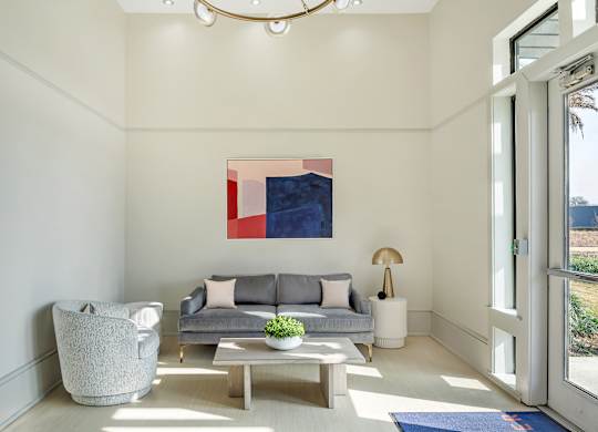 A modern living room with a grey couch, a grey armchair, a wooden coffee table, and a large abstract painting on the wall at The Addison,Louisiana 70836