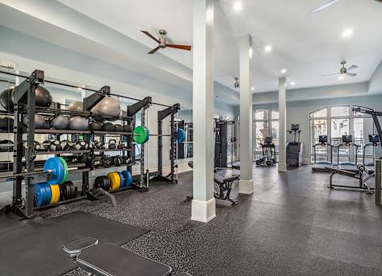 A gym with a variety of equipment including weight plates, weightlifting equipment, and a bench press at The Addison, Baton Rouge, Louisiana
