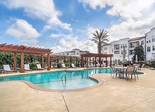 A pool surrounded by chairs and a wooden pergola at The Addison, Baton Rouge, LA 70836