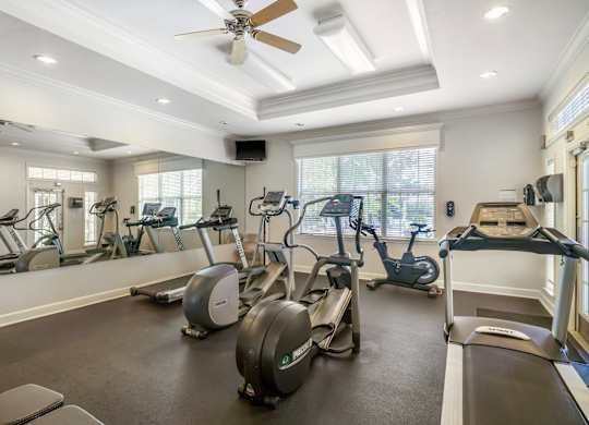 A spacious gym with a variety of exercise equipment and a ceiling fan.