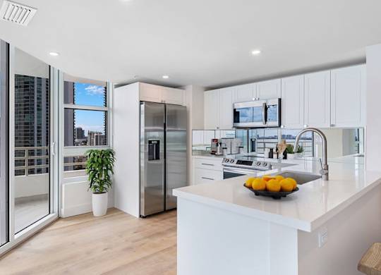 a white kitchen with a large island and a stainless steel refrigerator at The Hamilton, Florida