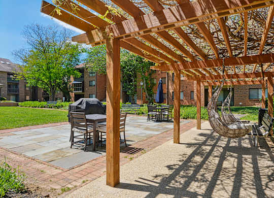 A wooden pergola provides shade over a patio with a table and chairs.