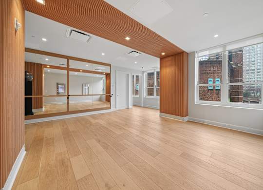 A spacious room with wooden floors and a large mirror on the wall.