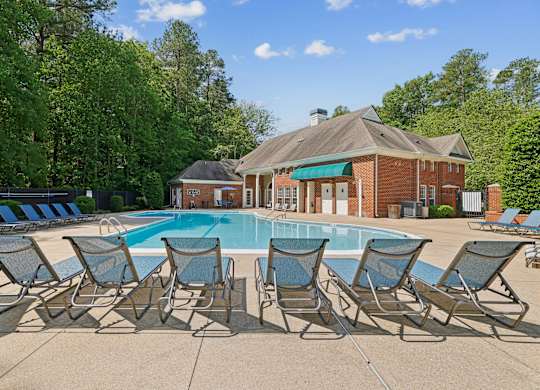 A pool surrounded by lawn chairs in front of a house.