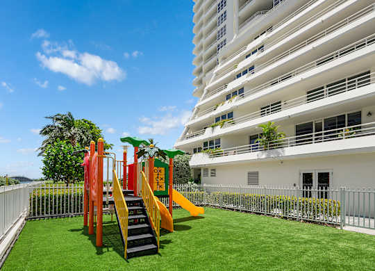 Outdoor childrens playground with colorful equipment and artificial turf at The Hamilton Apartments, Miami, FL 33137