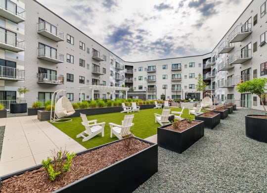an open courtyard with chairs and tables in front of an apartment buildingat Northern Lights a Lifestyle-Driven Community, West Fargo, 58078
