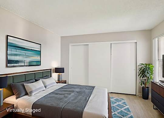 A bedroom with a bed, a painting, a lamp, a plant, and a TV.