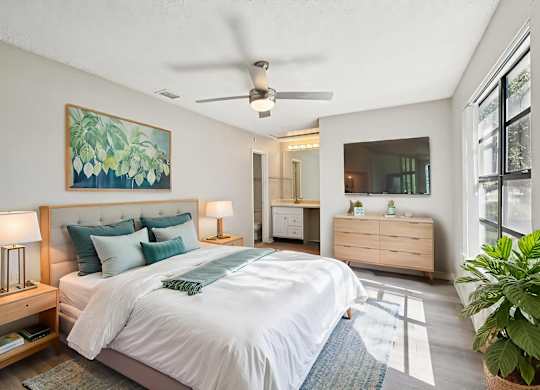 A bedroom with a large bed, a ceiling fan, and a painting on the wall.