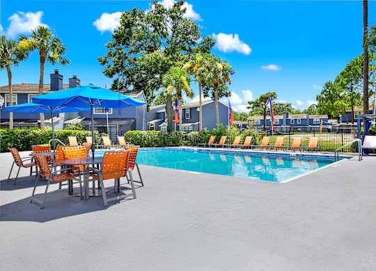 A pool area with a table and chairs and a blue umbrella.
