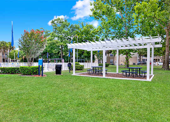 A white pergola with benches is situated in a grassy area.
