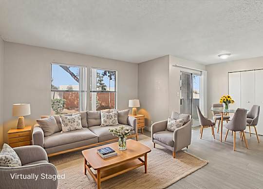 A living room with a grey couch, a wooden coffee table, and a dining table with chairs.