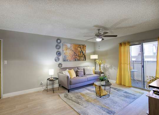 A living room with a grey couch, yellow curtains, and a ceiling fan.