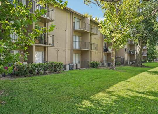 Apartment complex with green grass and trees in the foreground.