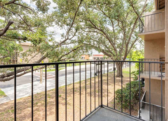 A balcony with a black railing overlooks a tree-lined street.