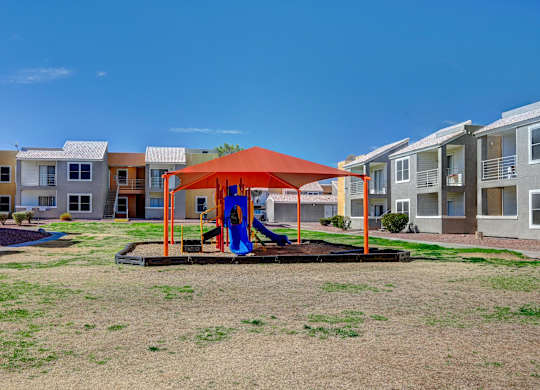 A playground with a red canopy and a blue slide in the middle of a grassy area.