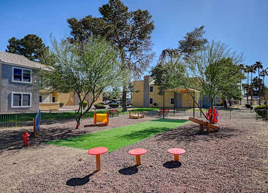 A playground with a red and orange play structure, a green lawn, and a red fire hydrant.