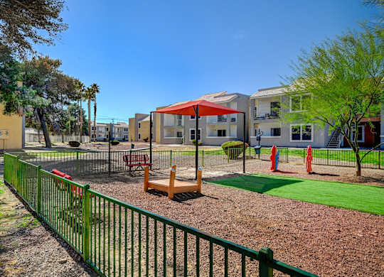A playground with a green fence and a red umbrella.