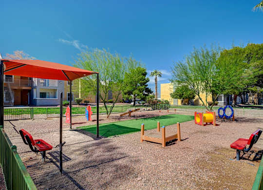 A playground with a red canopy and a green fence.
