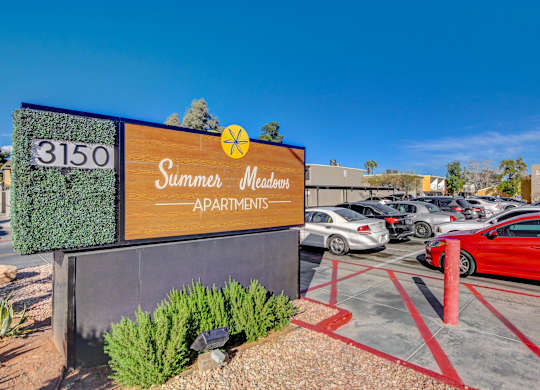 A sign for Summer Meadows Apartments with a parking lot in the background.