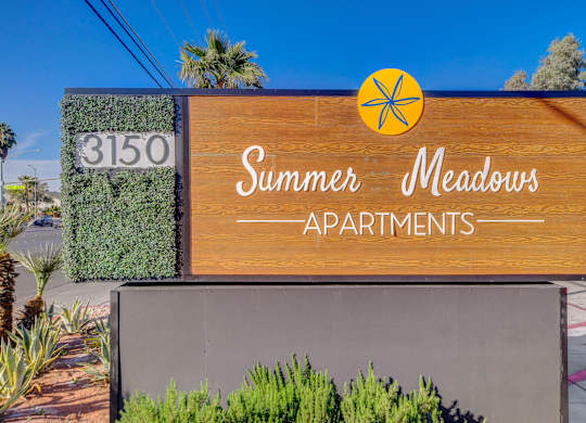 A wooden sign for Summer Meadows Apartments is displayed in front of a building.