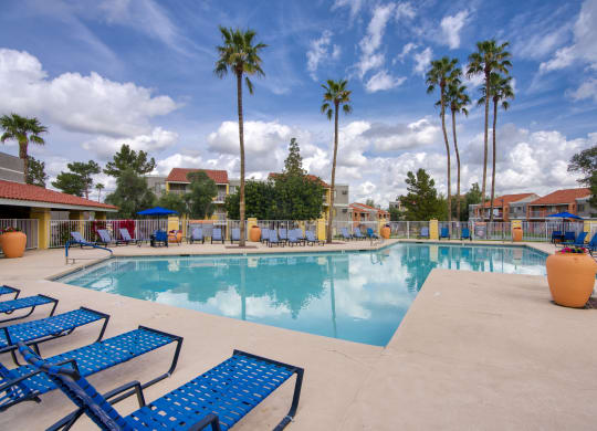 a large swimming pool with blue chaise lounge chairs and palm trees in the background at Valencia Park, Phoenix, AZ