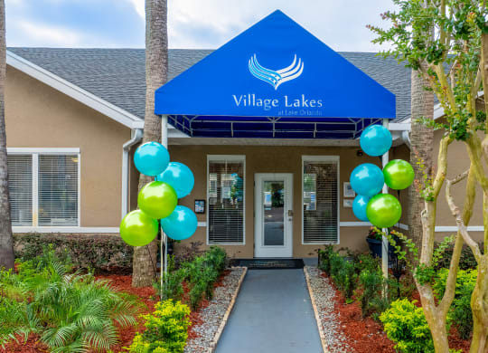 the front entrance to village lakes apartments with balloons and a blue roof at Village Lakes, Orlando, FL, 32808