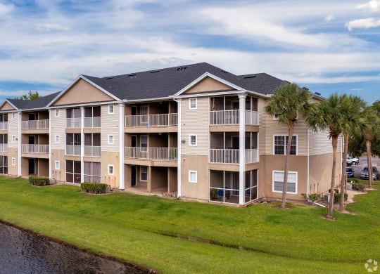 an apartment building with palm trees in front of a lake at Village Lakes, Orlando, FL, 32808