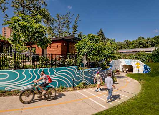 A person riding a bike on a concrete path with a blue and white mural on the wall.