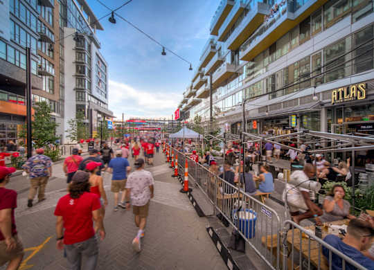 A busy street scene with people walking and sitting at outdoor tables.