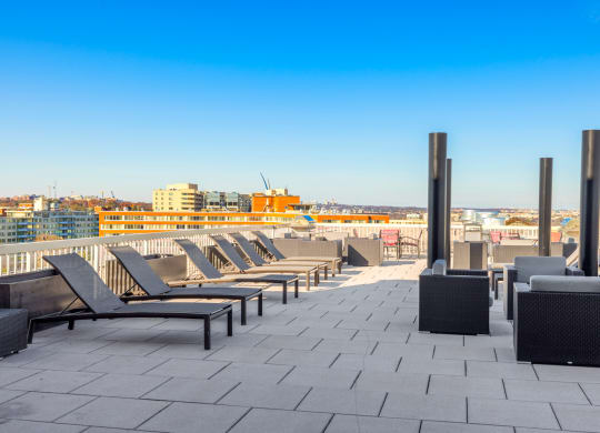 a row of lounge chairs on a rooftop patio overlooking the city