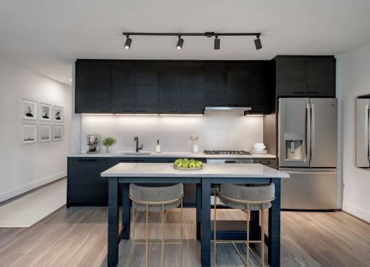 a kitchen with black cabinets and a blue island with three chairs at The Grace and Reva, Arlington, VA, 22202