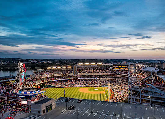 A baseball stadium is filled with fans and bathed in stadium lights.
