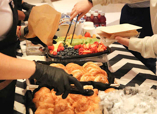 A person is serving food from a tray with a bag of chips.