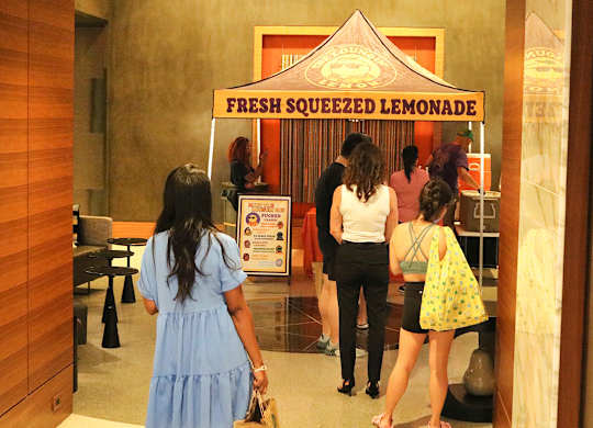 A group of people are standing in front of a lemonade stand.