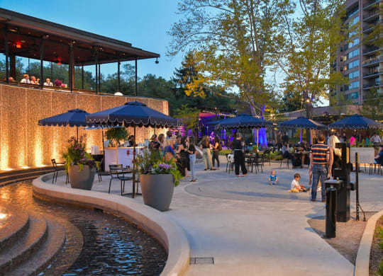 a crowd of people standing around a fountain and patio with umbrellas at The Grace and Reva, Arlington, 22202