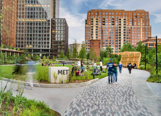 people walking around a park in a city with tall buildings