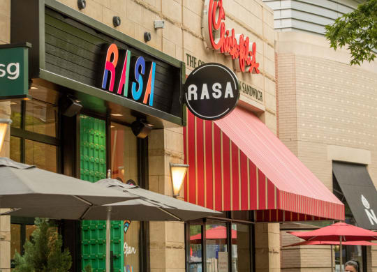 people walking outside of a restaurant with tables and umbrellas