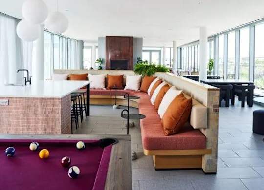 A billiard table is in the middle of a room with a long couch.